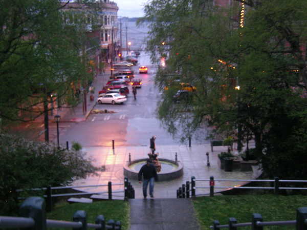 pedestrains walk around a fountain in a rainy streetscape